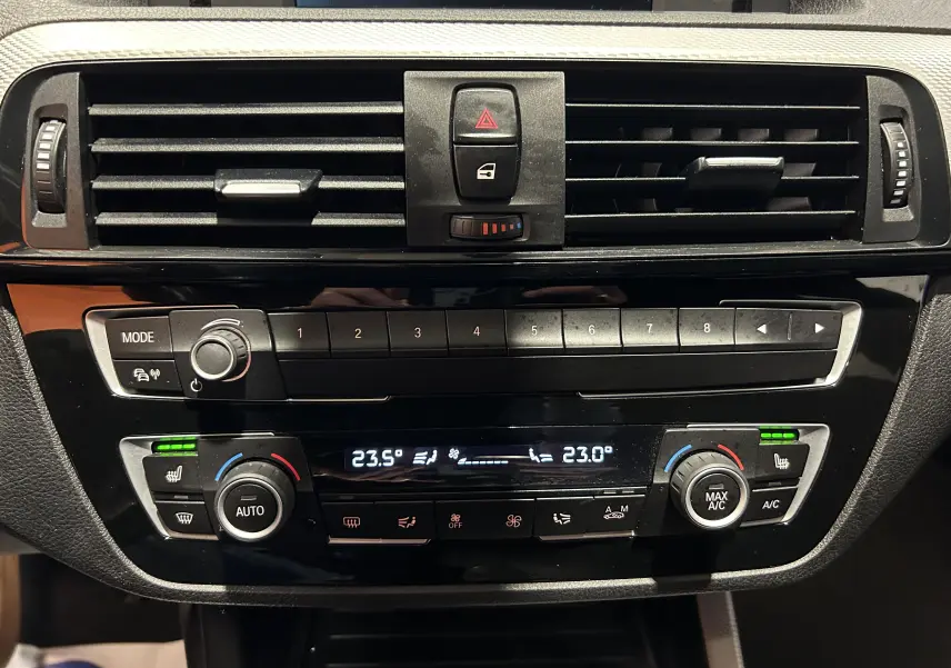 Tableau de bord de BMW Série 1 120iA 2019 montrant la console centrale avec commandes climatisation et sièges chauffants activés.