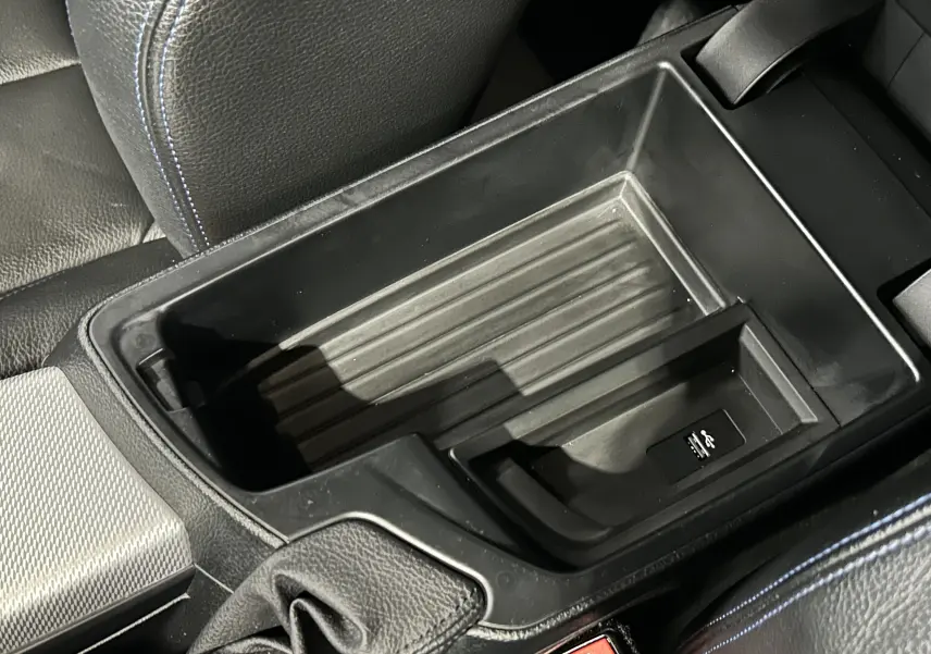 Gros plan sur le rangement central noir avec port USB, entouré de sièges en cuir noir à surpiqûres bleues de BMW Série 1 M Sport.