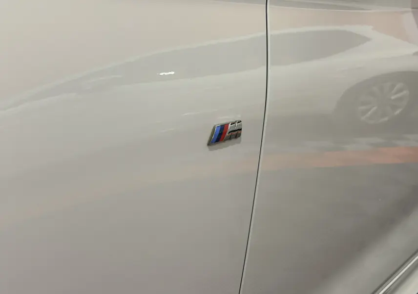Gros plan sur l'emblème M Sport coloré sur la porte blanche côté gauche d'une BMW Série 1 120iA 2019.