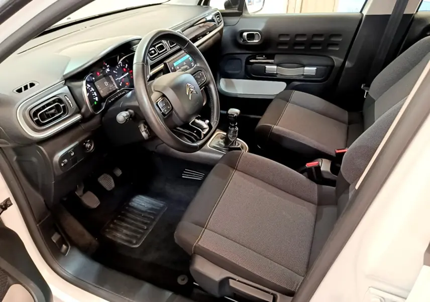 Vue intérieure côté conducteur de la Citroën C3 blanche 2019, volant cuir, tableau de bord et sièges gris foncé.