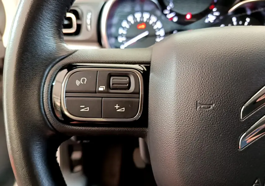 Gros plan sur le volant cuir noir de la Citroën C3 2019, avec commandes audio et tableau de bord flou en arrière-plan.