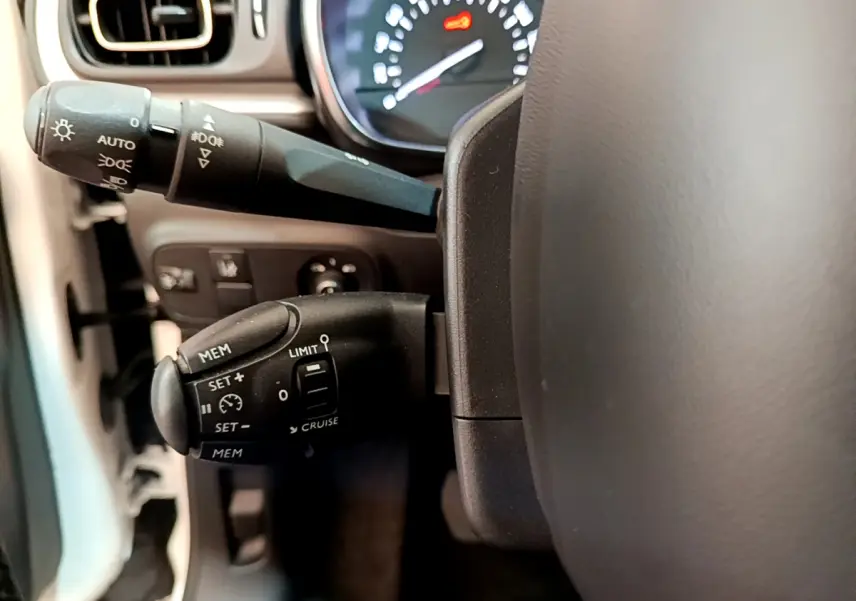 Gros plan sur la commande de régulateur de vitesse à gauche du volant dans l’habitacle d’une Citroën C3 blanche de 2019.