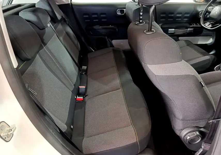 Vue intérieure côté gauche montrant la banquette arrière et siège avant tissu gris de la Citroën C3 blanche 2019.