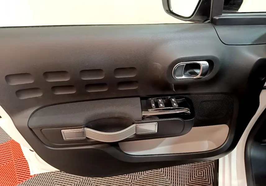 Vue intérieure du panneau de porte côté conducteur d'une Citroën C3 blanche, avec commandes de vitres et poignée noire.