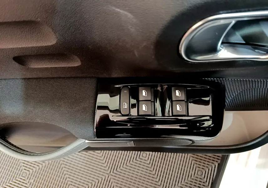 Gros plan sur les commandes des vitres électriques côté conducteur d'une Citroën C3 blanche de 2019.