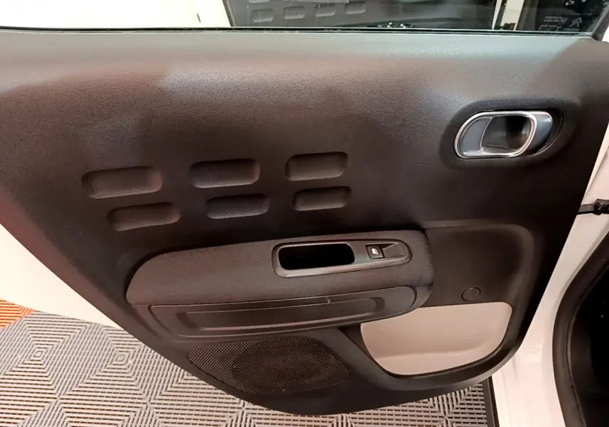 Gros plan sur la porte intérieure côté gauche noire et beige de la Citroën C3 blanche 2019, avec poignée chromée et bouton de vitre.