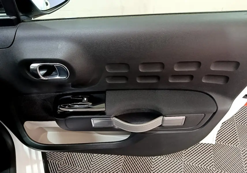 Vue rapprochée de la porte côté gauche d'une Citroën C3 blanche, avec poignée et commandes de vitres noires.