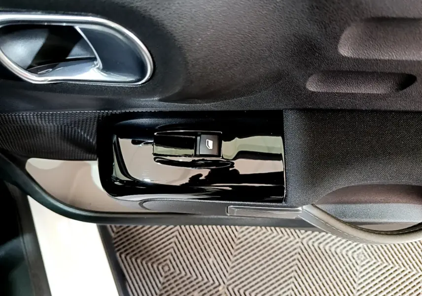 Gros plan sur la commande de lève-vitre côté gauche de la porte intérieure noire d'une Citroën C3 blanche 2019.