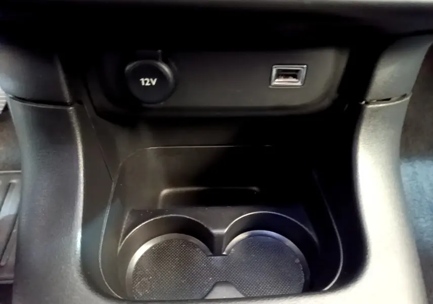 Gros plan sur la console centrale noire de la Citroën C3 avec prise 12V et port USB au-dessus des porte-gobelets.