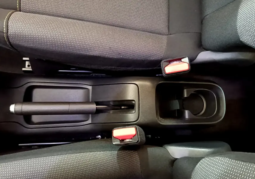 Vue plongeante sur la console centrale noire entre les sièges avant gris foncé de la Citroën C3 blanche.