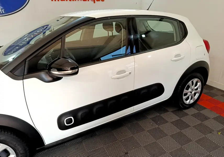 Profil côté gauche d'une Citroën C3 blanche avec protections noires caractéristiques sur les portières.