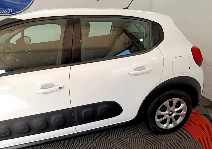 Profil côté gauche d'une Citroën C3 blanche avec protections latérales noires et jantes alliage visibles.