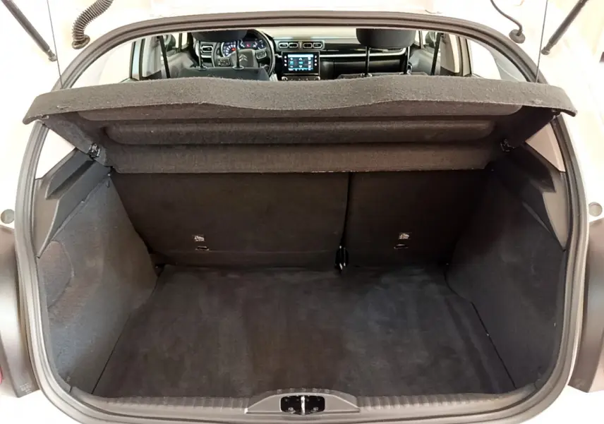 Coffre ouvert d'une Citroën C3 blanche 2019, vue intérieure vers l'avant avec tableau de bord et écran tactile visibles.