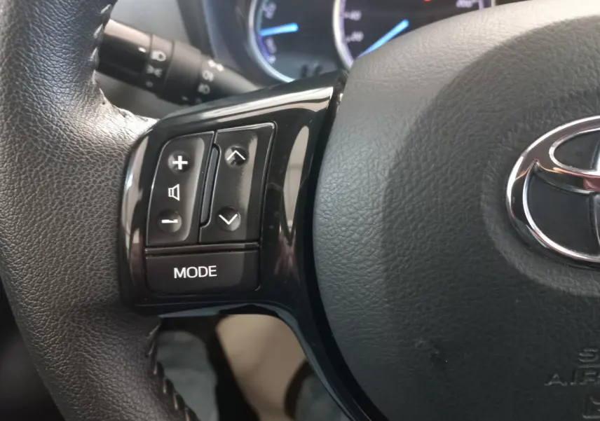 Gros plan sur les commandes gauche du volant en cuir noir de la Toyota Yaris 1.5 VVT-I HYBRID 2018.