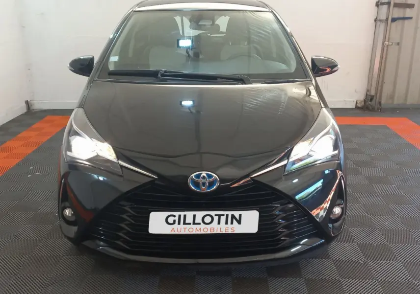 Vue frontale d'une Toyota Yaris noire 2018 avec phares allumés et calandre marquée en X dans un garage.