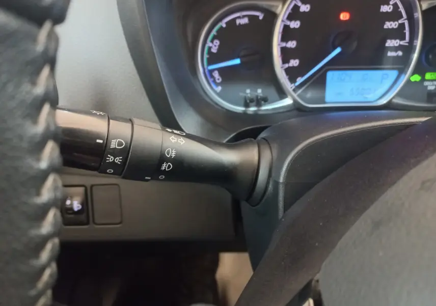 Gros plan sur la manette des phares à gauche du volant d'une Toyota Yaris hybride 2018, tableau de bord éclairé.