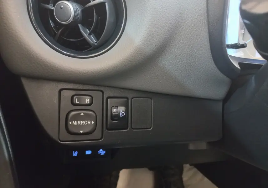 Détail des commandes de réglage des rétroviseurs et phares côté gauche dans l'habitacle de la Toyota Yaris noire 2018.