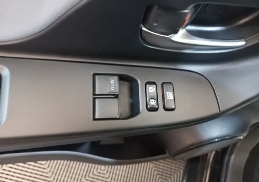 Gros plan sur la commande des vitres et verrouillage côté conducteur de la Toyota Yaris noire 2018, intérieur sobre.