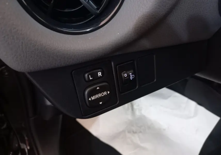 Gros plan sur les commandes de réglage des rétroviseurs et des phares d'une Toyota Yaris noire, côté conducteur.