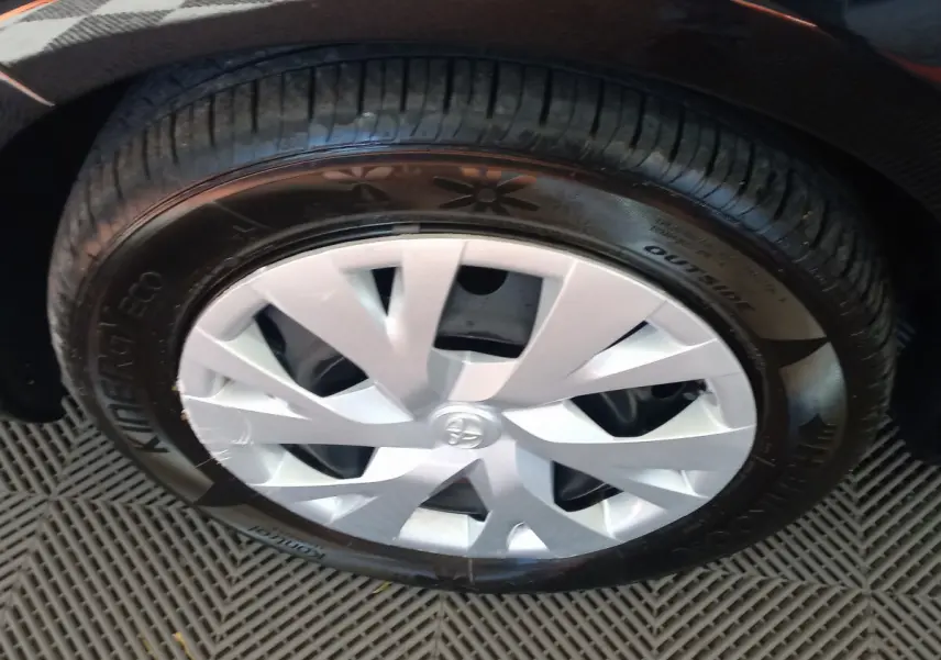 Gros plan sur la roue avant droite d'une Toyota Yaris noire, avec enjoliveur argenté et pneu Hankook.