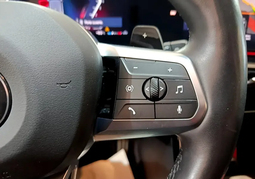 Gros plan sur les commandes du volant cuir noir du BMW X1 xDrive23i M Sport 2023, boutons multifonctions visibles.