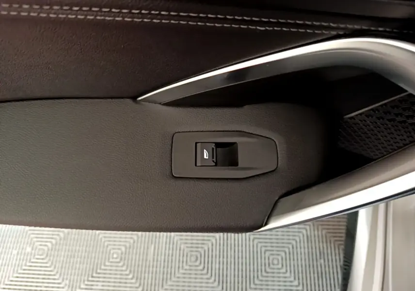 Gros plan sur la commande de vitre électrique intégrée dans la garniture noire de la porte côté conducteur du BMW X1 gris clair 2023.