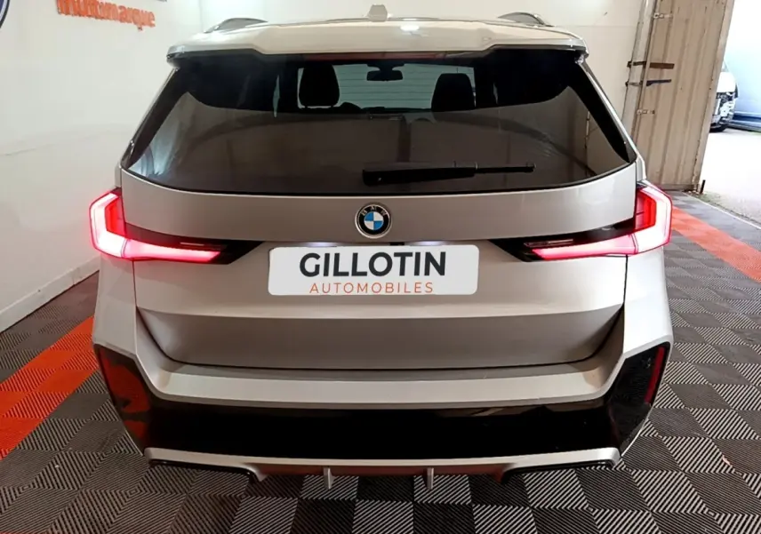 Vue arrière d'un BMW X1 gris clair avec feux LED allumés dans un garage intérieur.