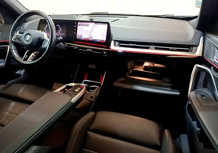 Vue intérieure avant droite du BMW X1 xDrive23i M Sport 2023, tableau de bord moderne avec écran tactile et éclairage d'ambiance rouge.