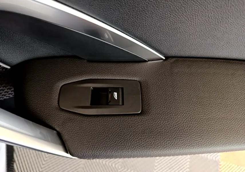 Détail du bouton de commande de la vitre sur la porte intérieure noire d’un BMW X1 xDrive23i M Sport gris clair.