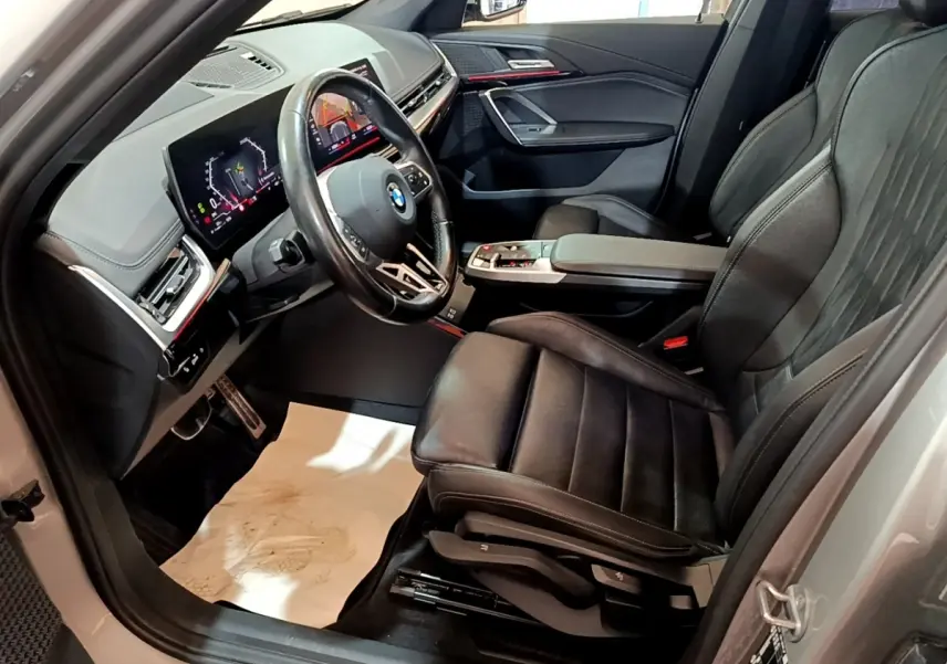 Vue intérieure côté conducteur du BMW X1 xDrive23i M Sport 2023, sièges cuir noirs et tableau de bord digital lumineux.