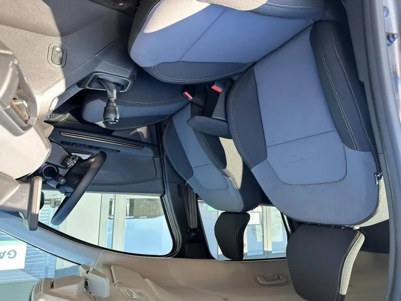 Vue intérieure côté conducteur du Dacia Jogger blanc, montrant les sièges avant noirs avec coutures contrastantes et levier de vitesse manuel.