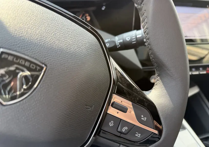 Gros plan sur le volant cuir noir de la Peugeot 308 2025 avec commandes intégrées et logo visible.