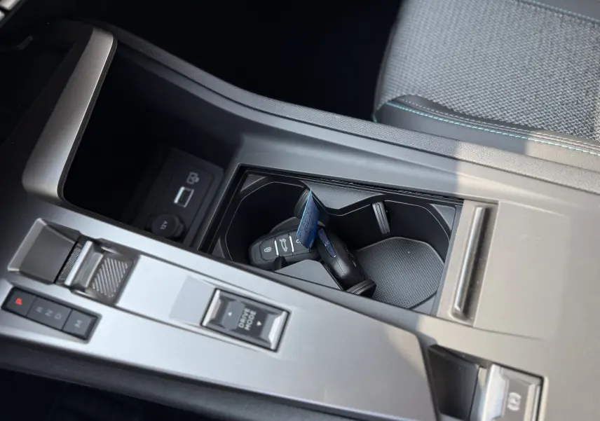 Gros plan sur la console centrale grise de la Peugeot 308 2025 avec clés dans porte-gobelets et commandes de boîte auto.