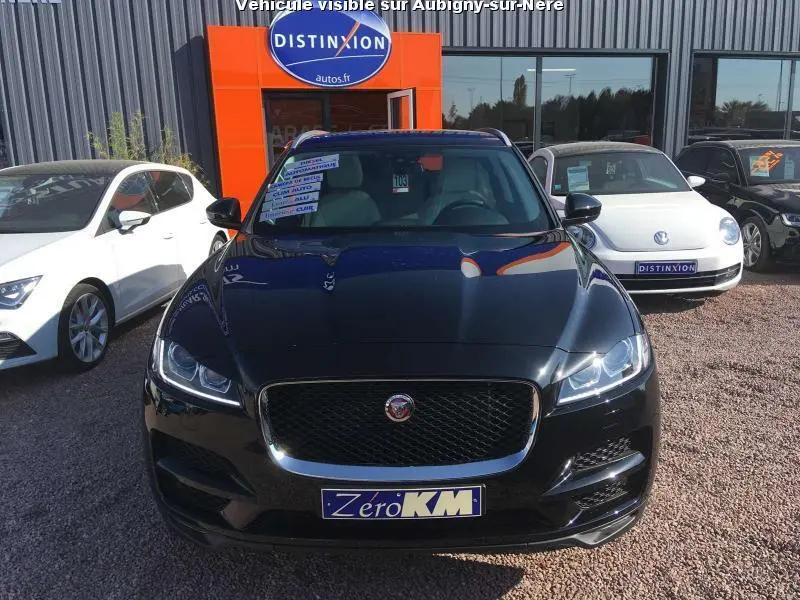 Jaguar F-PACE noir vue de face, avec calandre chromée et phares LED adaptatifs allumés, sur parking extérieur.