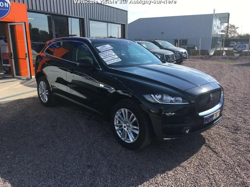 Jaguar F-PACE noir en 3/4 avant droit, jantes argentées, vitres surteintées, garé devant un bâtiment commercial.