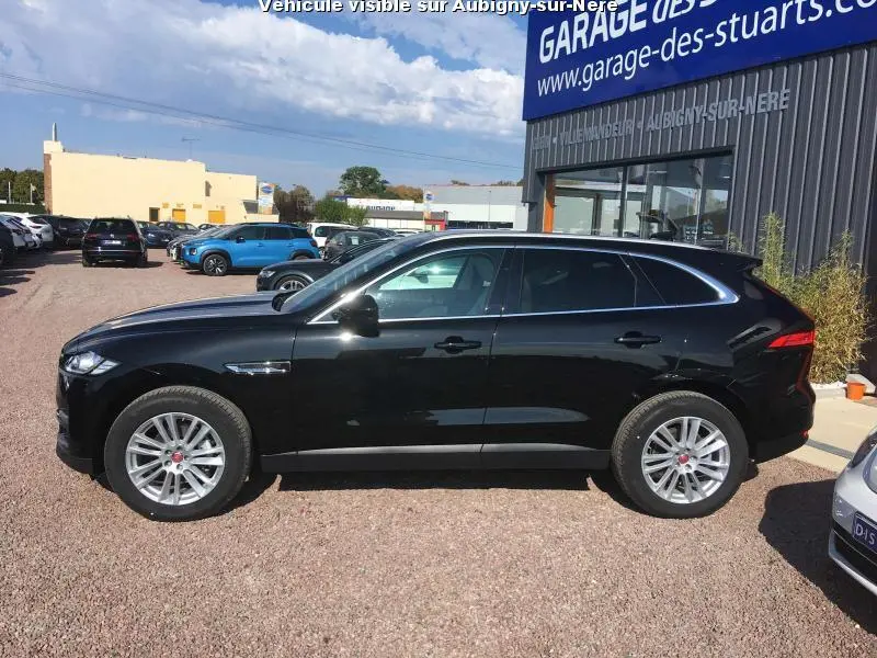 Profil droit d'un Jaguar F-PACE noir 2018 garé devant un garage, avec jantes argentées et vitres teintées.