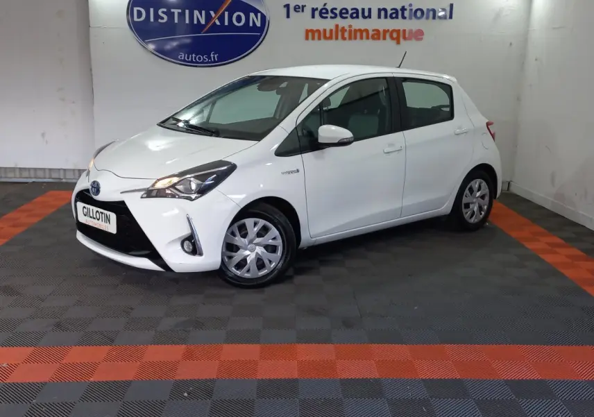 Toyota Yaris hybride blanche vue de profil avant droit dans un showroom avec logo Distinxion en arrière-plan.