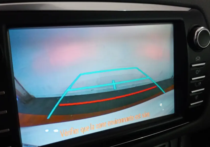 Vue de la caméra de recul de la Toyota Yaris blanche, affichant les lignes de guidage sur l'écran tactile du tableau de bord.