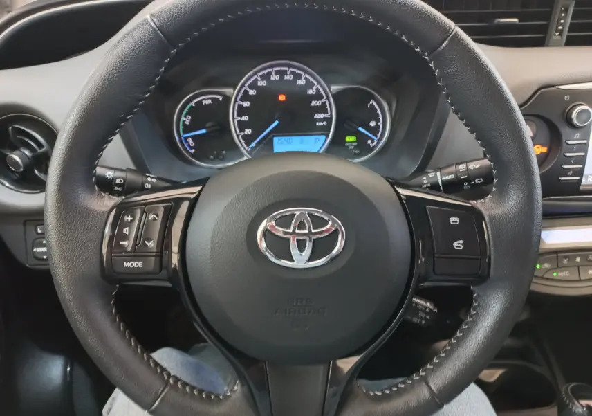 Vue rapprochée du volant cuir noir de la Toyota Yaris 2019 avec commandes multifonctions et tableau de bord lumineux.