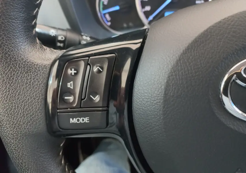 Gros plan sur les commandes gauche du volant en cuir noir de la Toyota Yaris hybride 2019, avec logo Toyota visible.