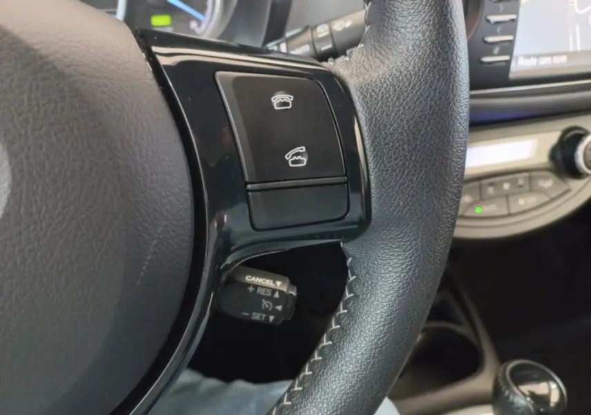 Gros plan sur la partie droite du volant noir en cuir de la Toyota Yaris hybride, avec commandes téléphoniques et régulateur de vitesse.