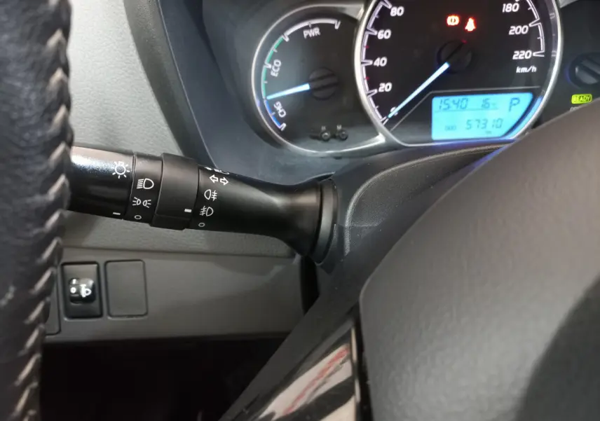 Gros plan sur le tableau de bord et la manette des phares de la Toyota Yaris hybride blanche, affichage digital visible.