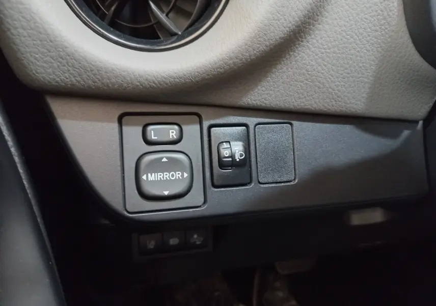 Gros plan sur les commandes de réglage des rétroviseurs et des phares dans une Toyota Yaris blanche 2019.