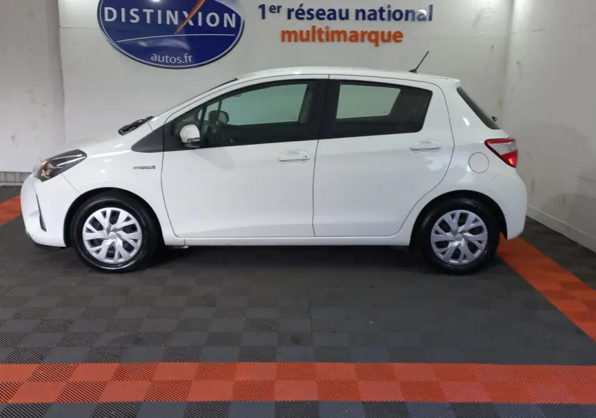 Profil côté gauche d'une Toyota Yaris blanche hybride 2019, avec jantes standard et logo Hybrid visible sur l'aile avant.