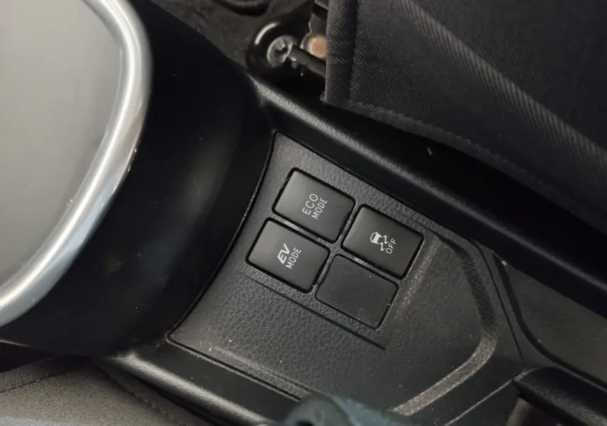Gros plan sur les boutons de modes de conduite et contrôle de stabilité dans l'habitacle noir d'une Toyota Yaris hybride blanche.