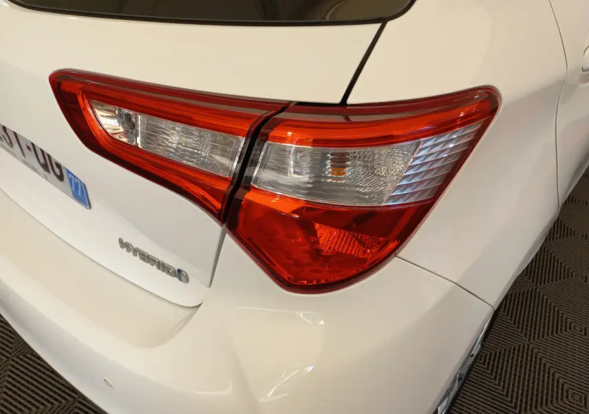 Gros plan sur le feu arrière droit d'une Toyota Yaris hybride blanche, avec logo Hybrid visible sur le coffre.