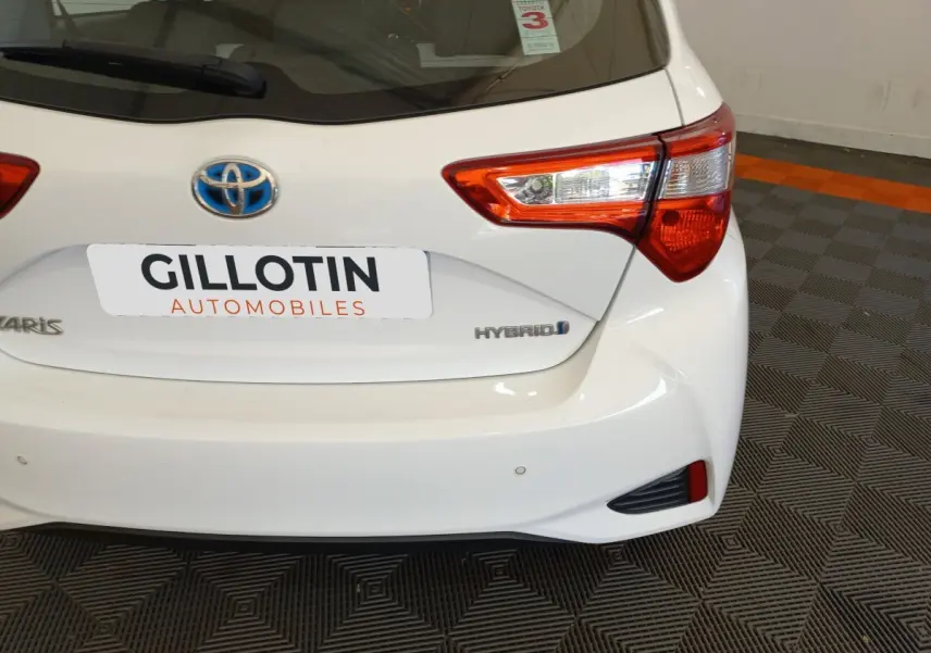 Vue arrière droite d'une Toyota Yaris blanche hybride 2019 avec feux arrière distinctifs et logo bleu Toyota.