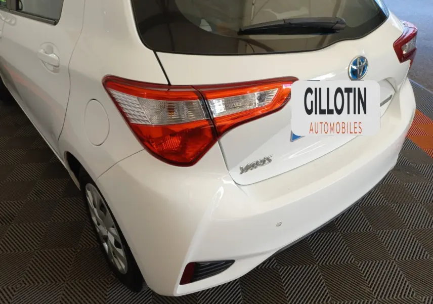 Vue 3/4 arrière droite d'une Toyota Yaris blanche, mettant en valeur les feux arrière et le logo Toyota sur le hayon.