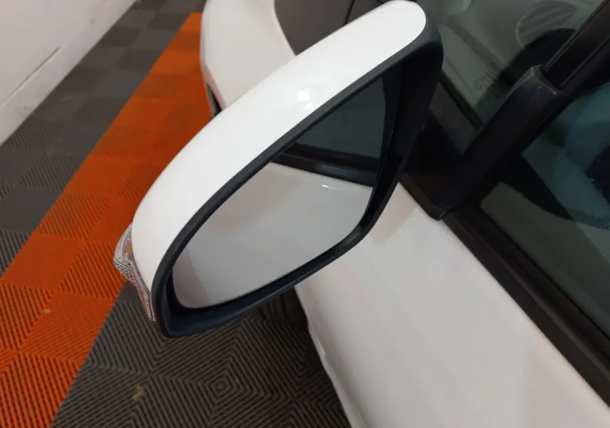 Rétroviseur côté gauche blanc de la Toyota Yaris 2019 hybride, avec clignotant intégré visible sur fond de sol orange et gris.