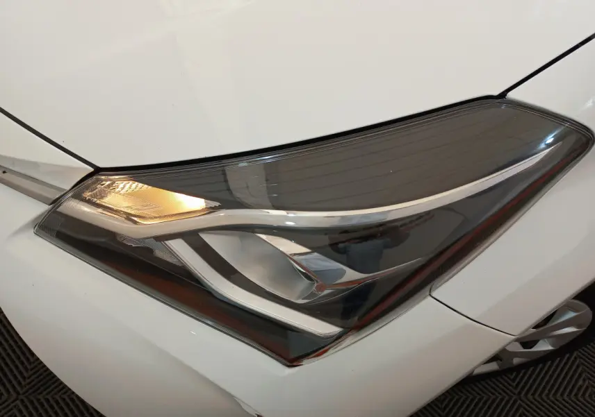 Gros plan sur le phare avant gauche allumé d'une Toyota Yaris blanche 2019 version hybride France Business.